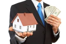 A businessman holds a house in one hand and money in another.